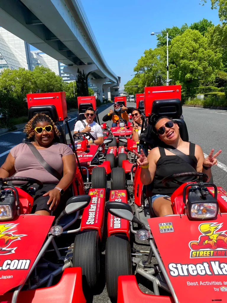 Group of friends riding bright red Street Kart go-karts on a sunny city street, posing for the camera under an elevated track.